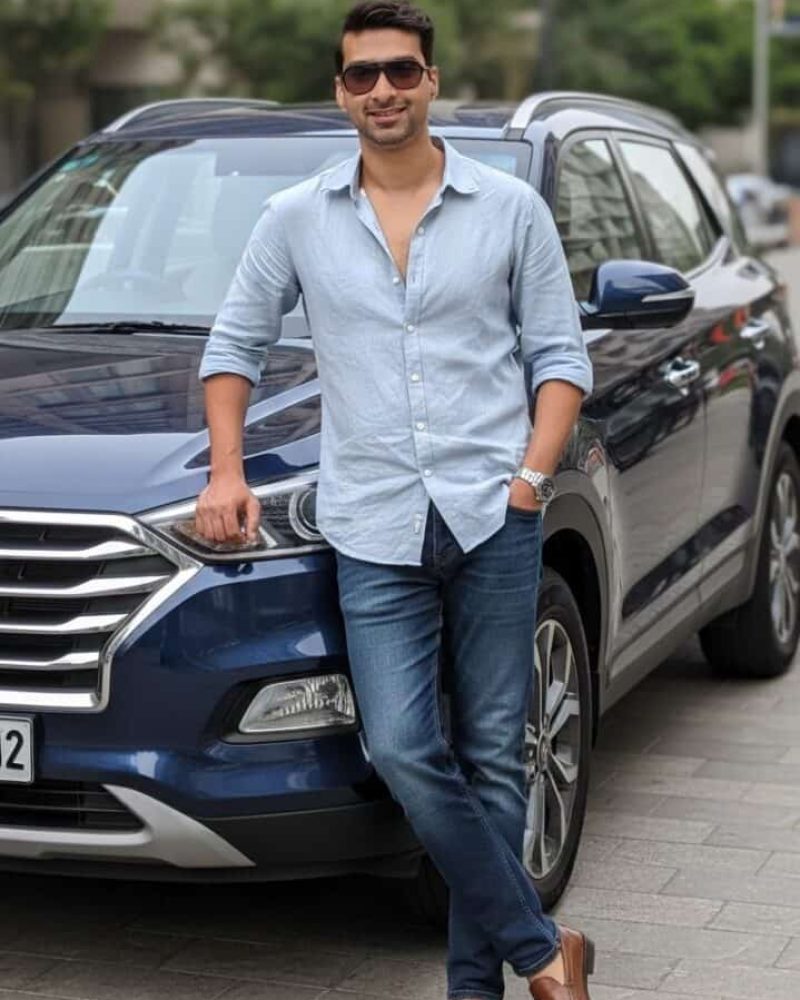 Stylish man in casual wear leaning on a blue SUV for car purchase or rental service.